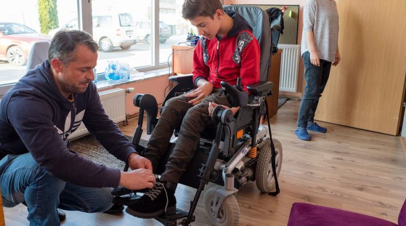 In Kosovo, a father helps his son, who suffers from cerebral palsy, get back into his electric wheelchair.